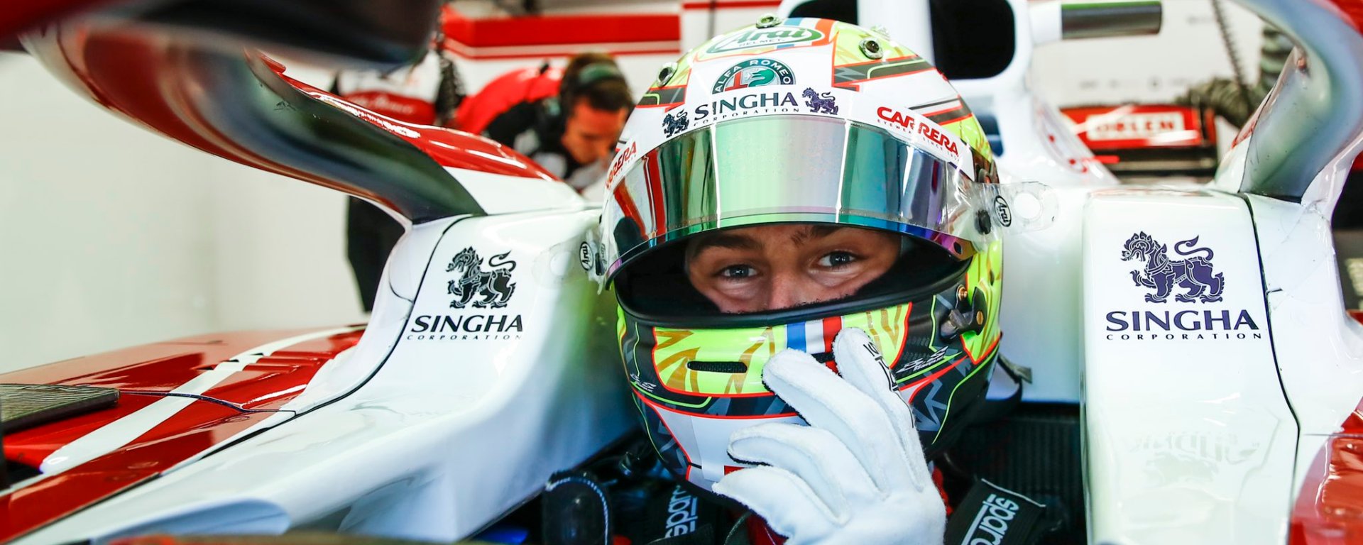 Driver with yellow, black and red helmet seated in car cockpit, facing the camera