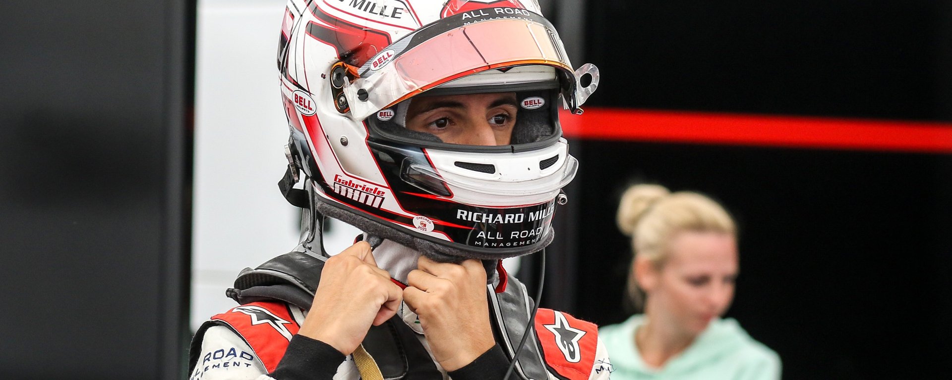 Man in white and red racing suit and helmet undoing helmet straps looking to the right of the camera.