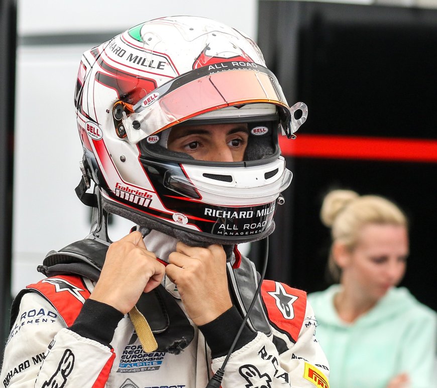 Man in white and red racing suit and helmet undoing helmet straps looking to the right of the camera.