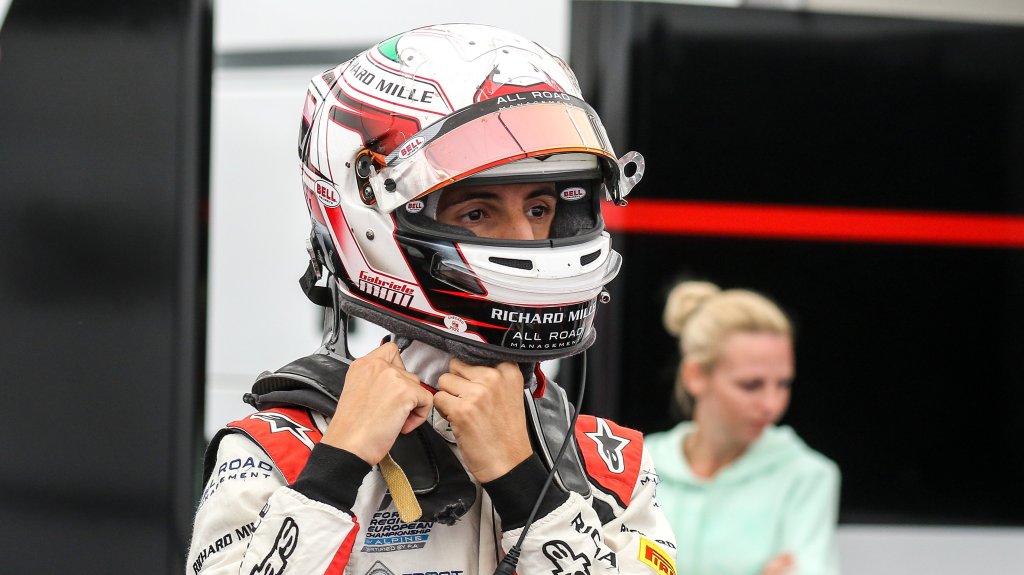 Man in white and red racing suit and helmet undoing helmet straps looking to the right of the camera.