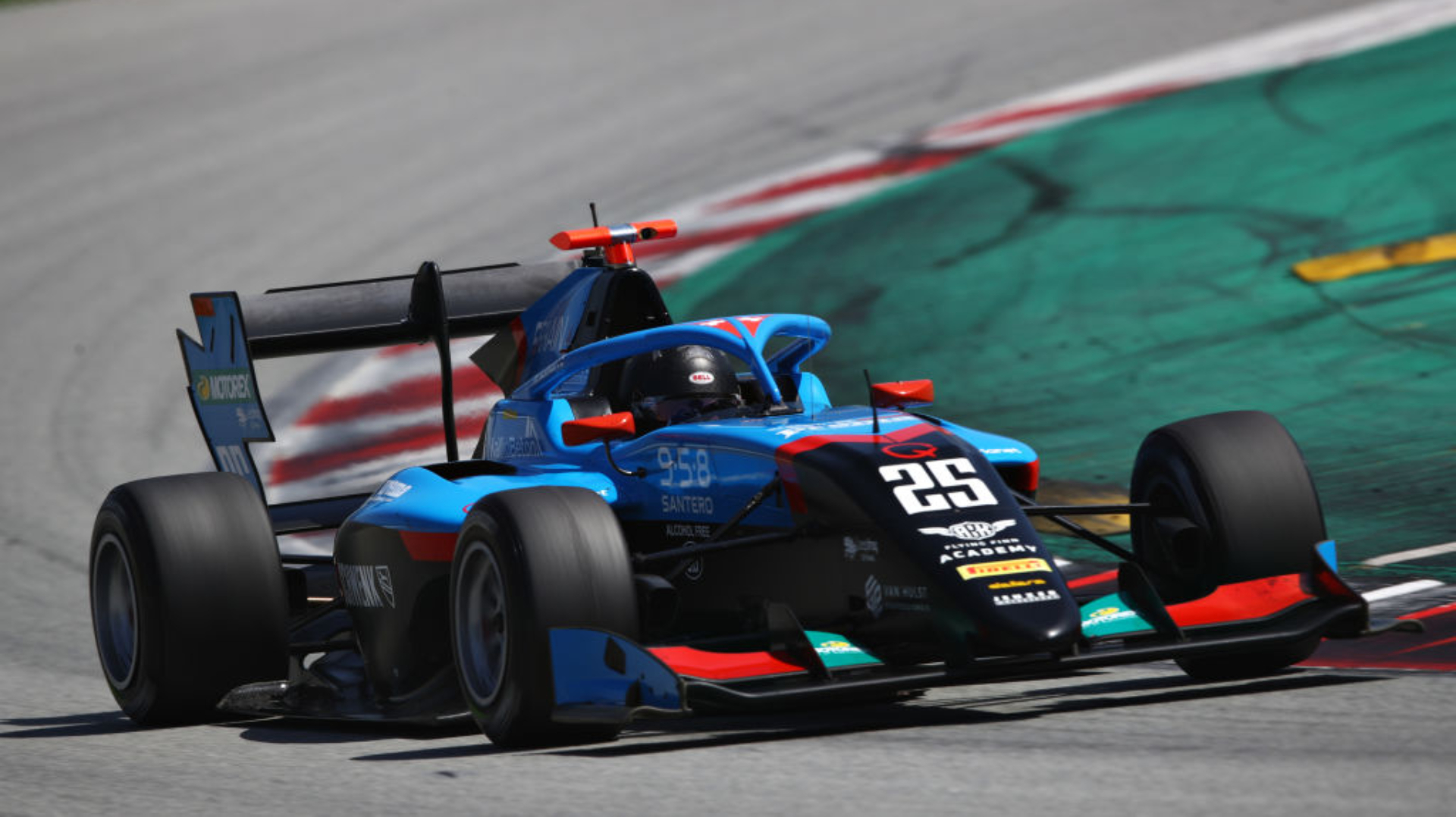 Blue and red Formula 3 car driving to the right of the camera with red and white kerb on its left