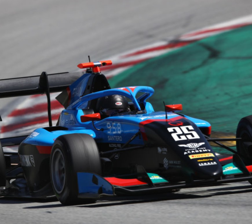 Blue and red formula 3 car driving to the right of the camerawith red and white kerb on its left.