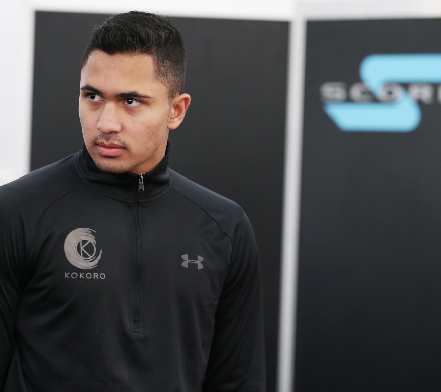 A boy with black hair and a black Under Armour jacket with the Kokoro Performance logo stands in front of a black background with the Scorpio Motorsport logo