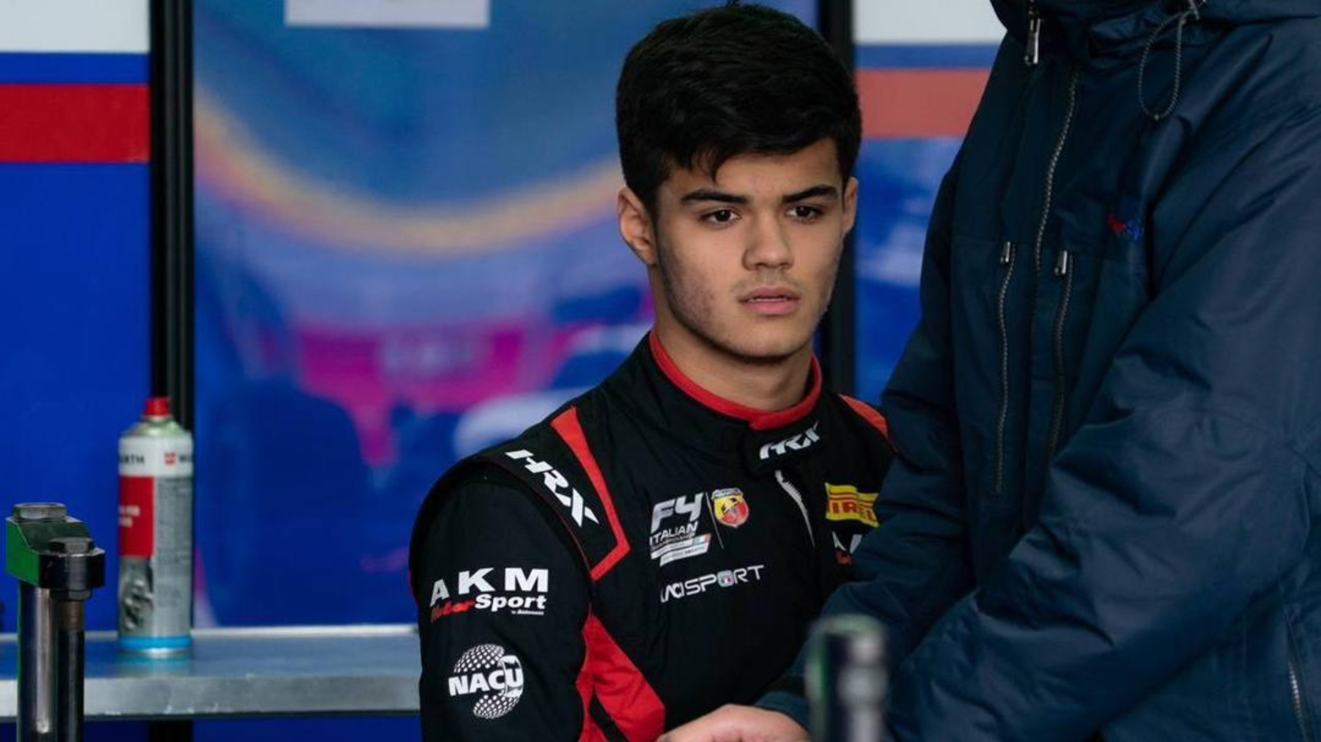 Man in black and red racing suit looking towards the camera and down.