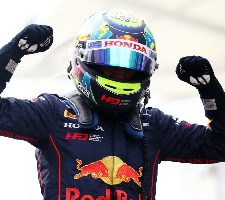 Ayumu Iwasa, wearing his neon yellow and blue helmet and his blue Red Bull–branded racing suit, lifts both fists in celebration