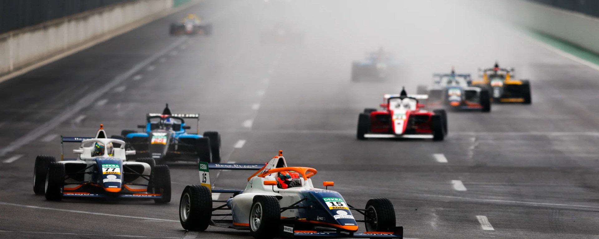 Cars turn left at the Lausitzring as spray from a previous rainstorm blankets the main straight