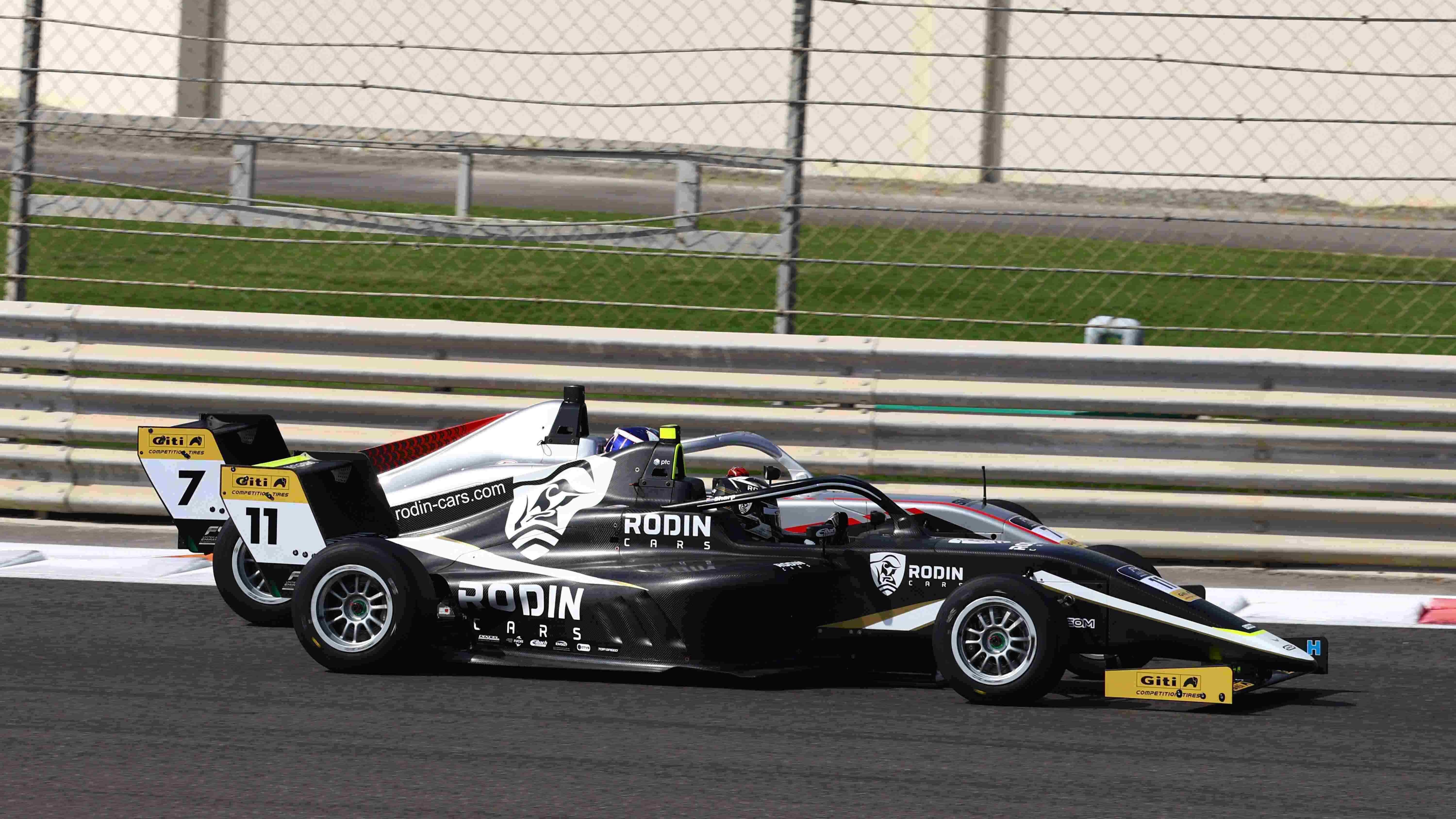 A black car (Louis Sharp, #11) holds a slight advantage over the silver car (Alex Dunne, #7) on the inside of Turn 9, the long, sweeping left-hander at Yas Marina Circuit. The kerbing and the Armco barrier are in the background, behind Dunne's car.