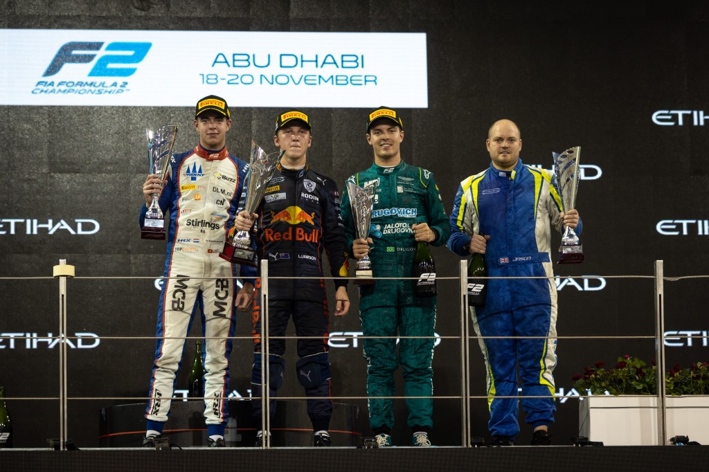 Richard Verschoor, Liam Lawson, Felipe Drugovich and Carlin mechanic Jason Cox stand on the podium at the Yas Marina Circuit, holding their trophies and podium champagne aloft