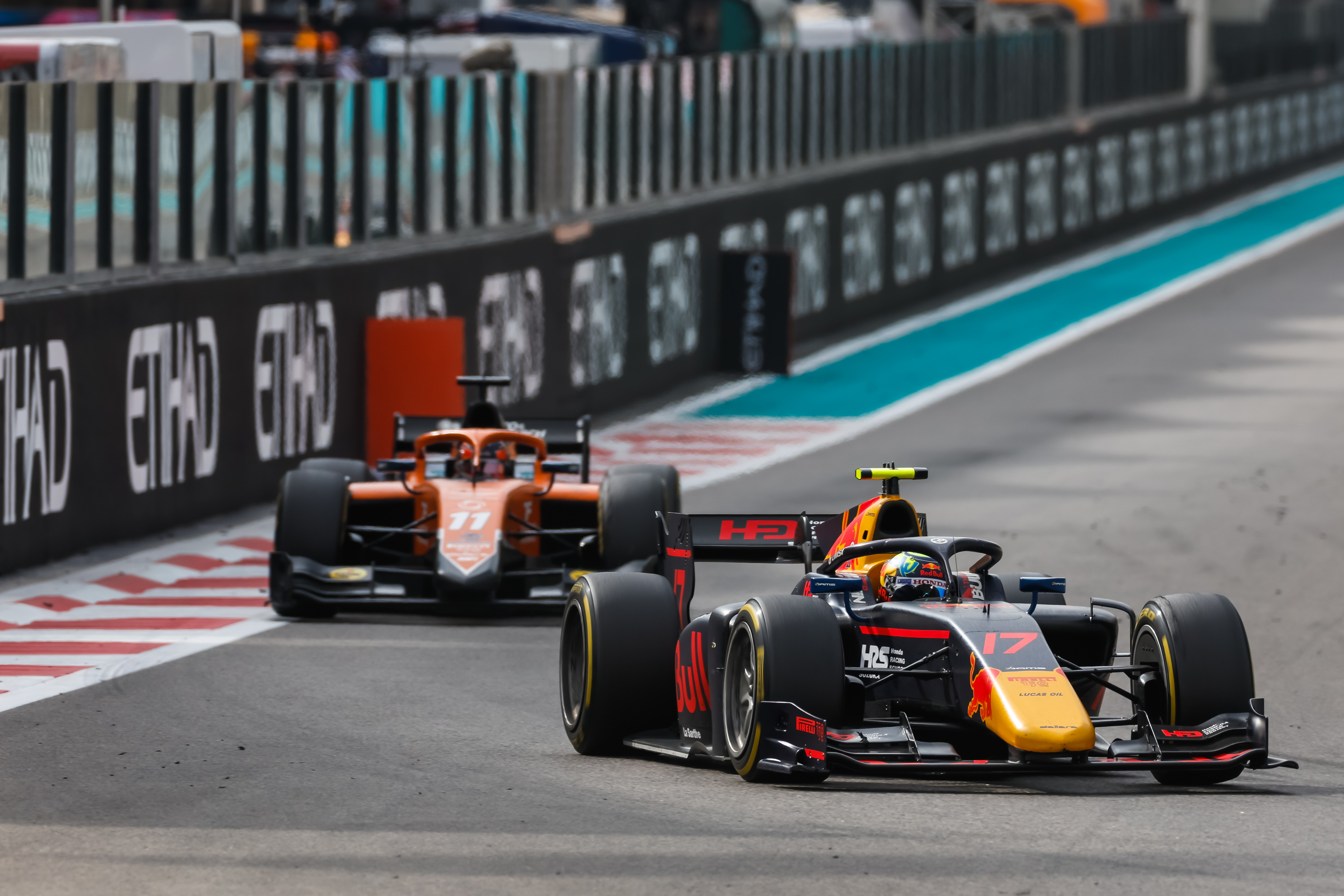 The Red Bull–sponsored DAMS F2 car of Ayumu Iwasa makes a left turn to the right of the foreground as the orange and black MP Motorsport car of Felipe Drugovich in the background prepares to make the same manoeuvre