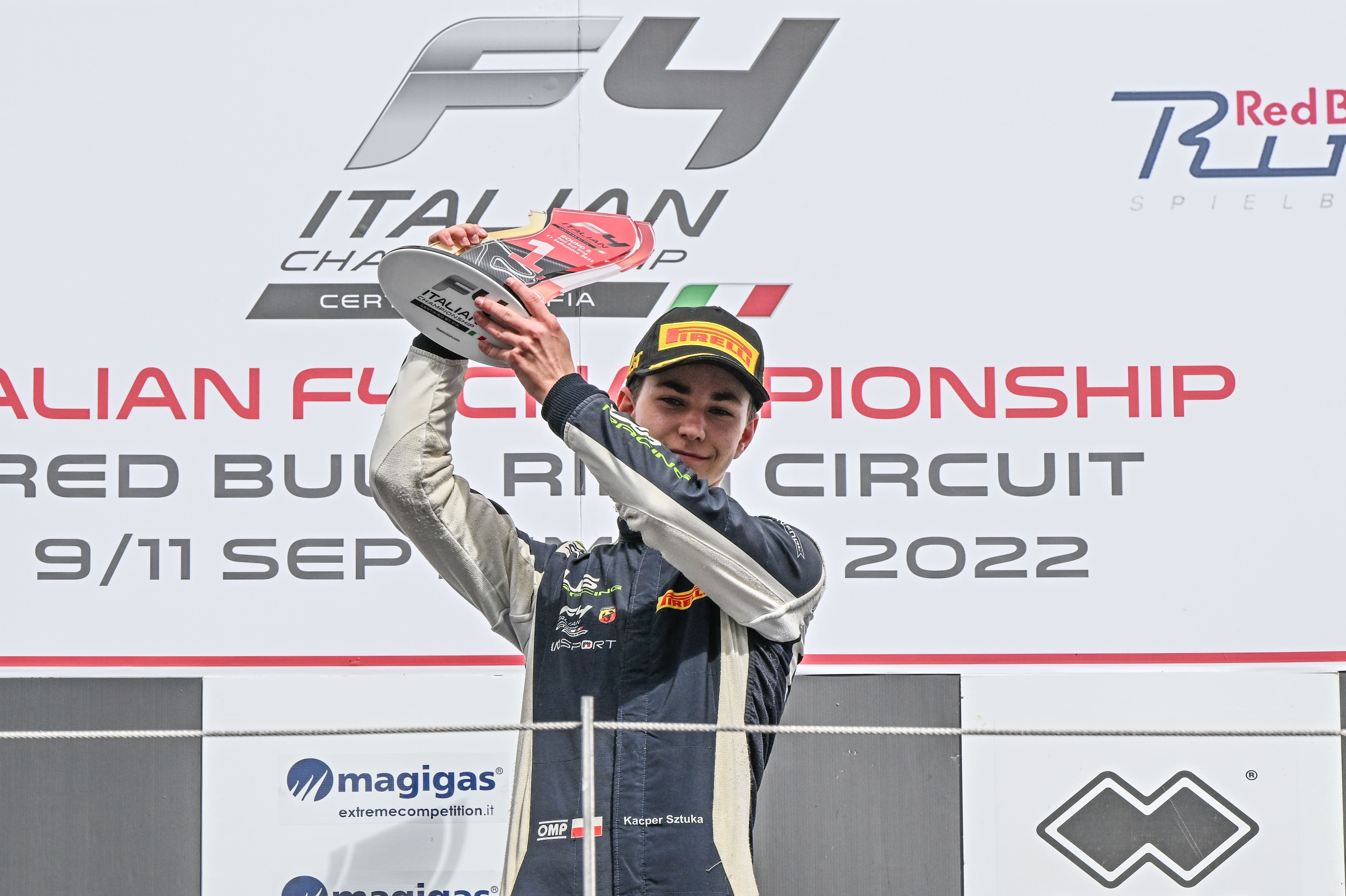 Kacper Sztuka on the podium, holding a first-place trophy with both hands. The text behind him reads "Italian F4 Championship: Red Bull Ring Circuit, 9/11 September 2022"