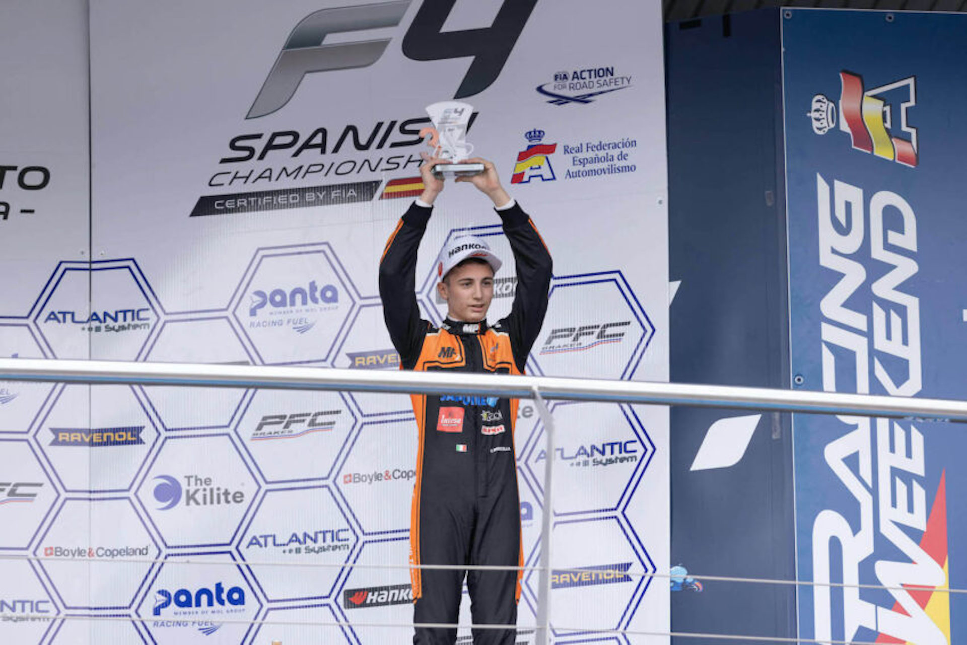 Valerio Rinicella holds a trophy aloft with both hands. The F4 Spanish Championship, FIA Action for Road Safety, and Real Federación Española de Automovilismo logos appear behind him.