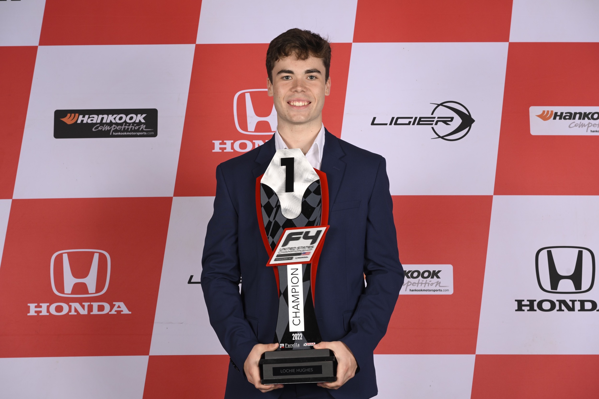 Lochie Hughes holds a gray, black and red trophy reading "F4 United States Championship powered by Honda: Champion 2022.
