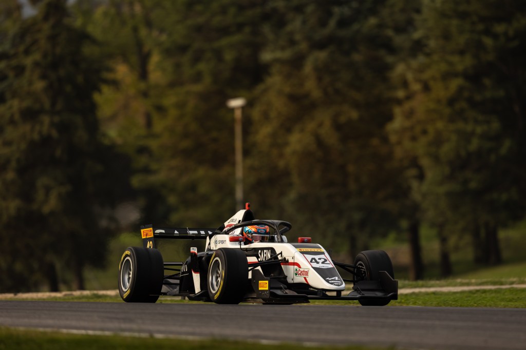 A white and black car drives to the left with greenery behind