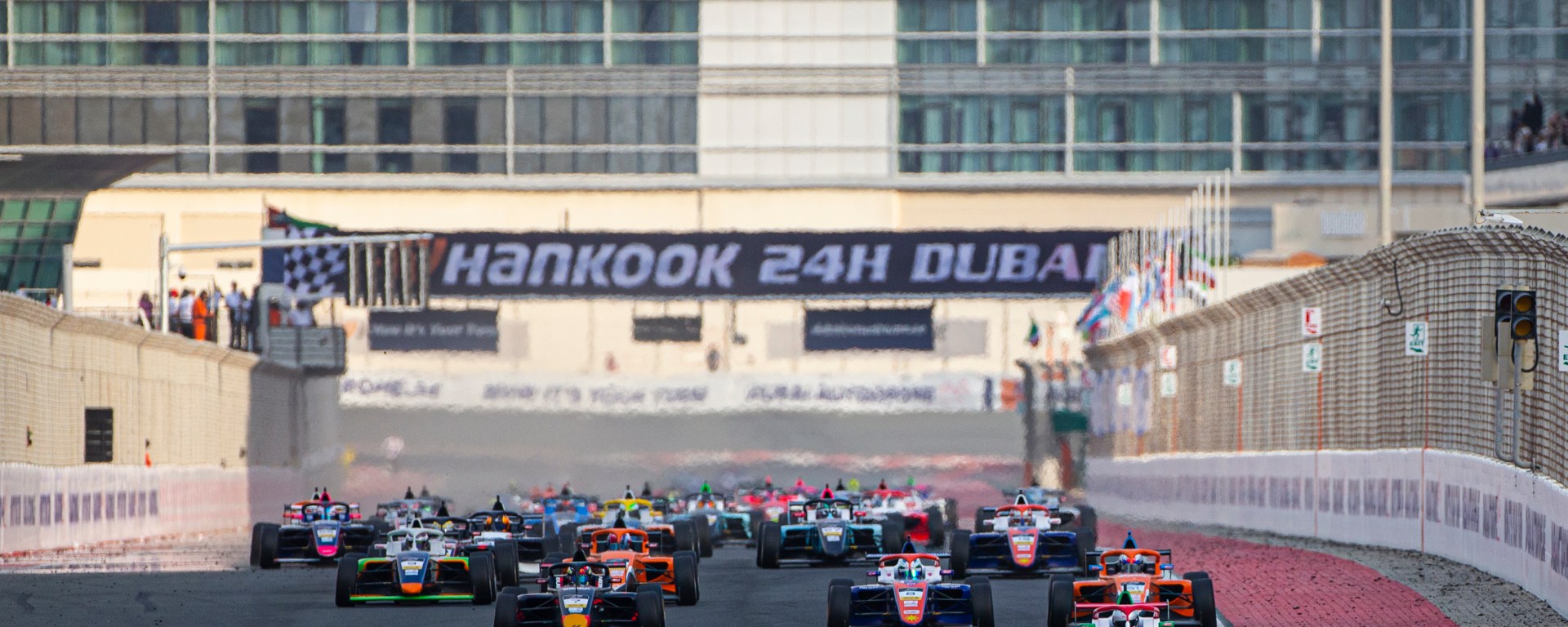 A grid of 39 cars races down the front straight of the Dubai Autodrome with "Hankook 24H Dubai" in the background on the signage