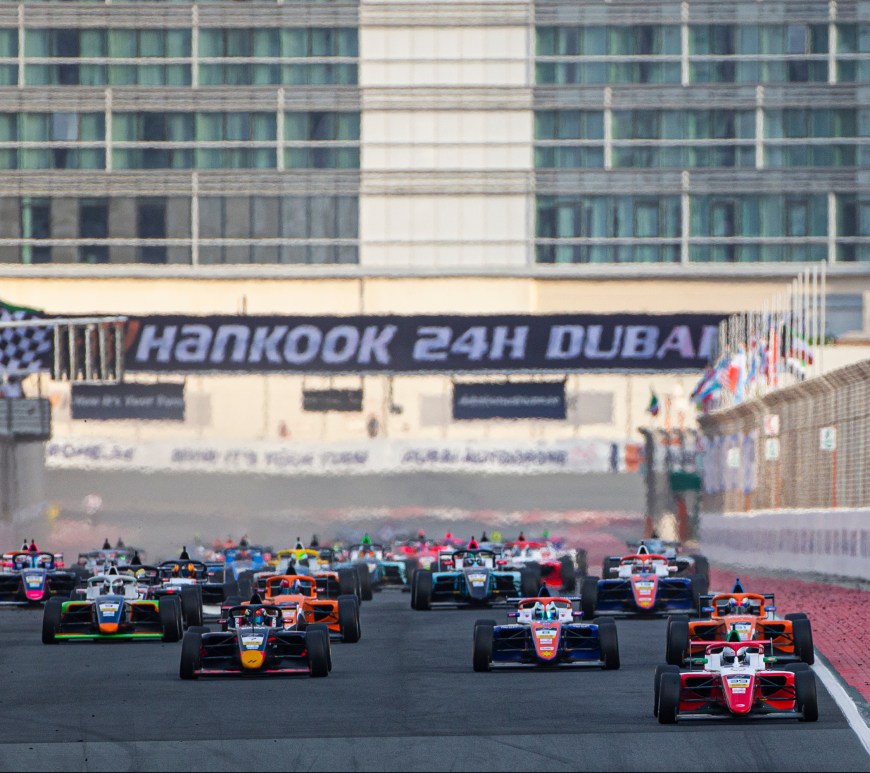 A grid of 39 cars races down the front straight of the Dubai Autodrome with "Hankook 24H Dubai" in the background on the signage