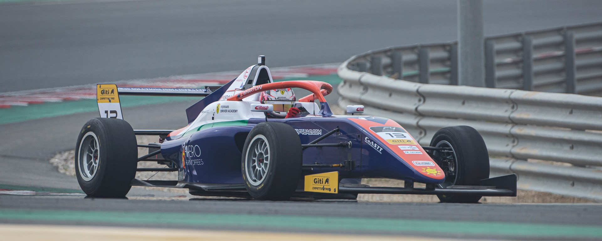 A blue, orange, white and green car navigates a left turn, photographed from the right side
