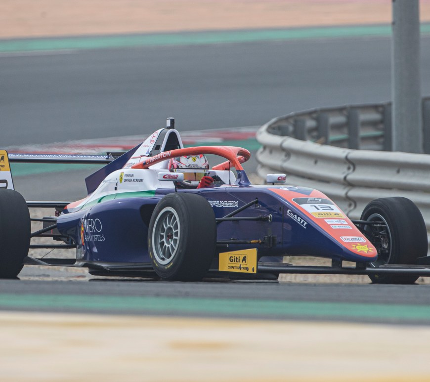 A blue, orange, white and green car navigates a left turn, photographed from the right side