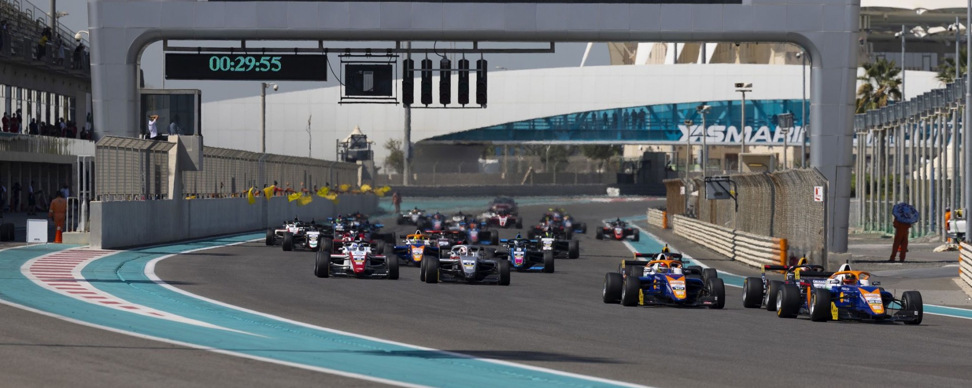 Cars make a slight left on the Yas Marina Circuit along the back straight, with the clock reading 29:55 and the Yas Marina Circuit logo in the background