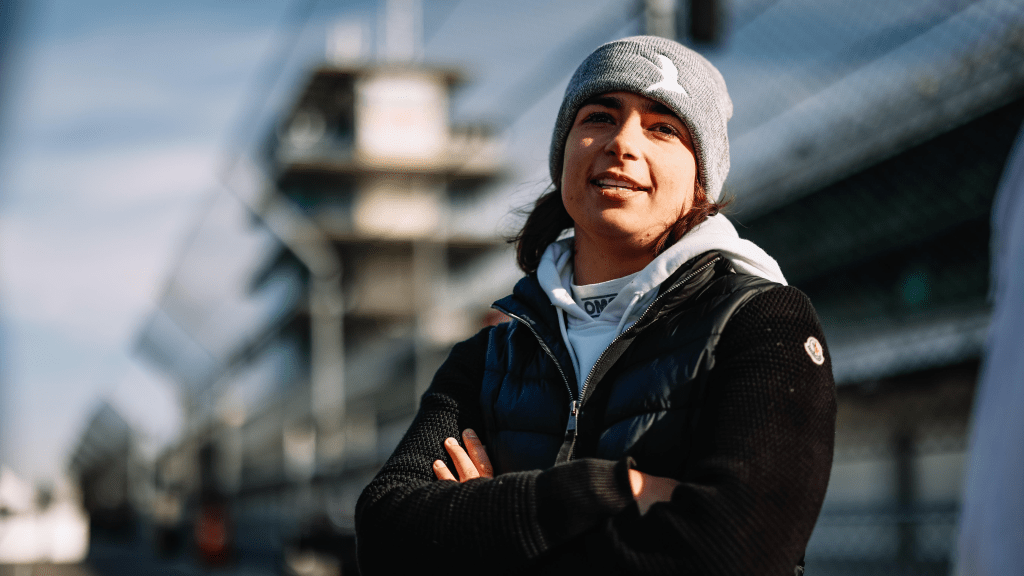 Jamie Chadwick wearing a beanie and a coat with her arms folded smiling at the camera