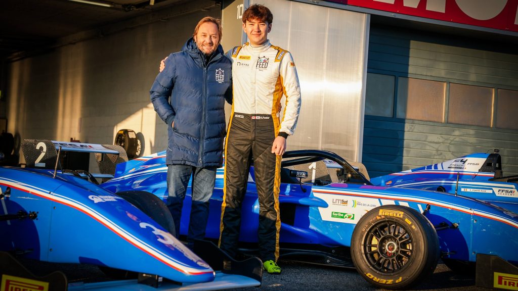 Patrick Lemarié, wearing a FEED Racing coat, puts his arm around Kevin Foster, wearing FEED Racing overalls. They stand amongst blue French F4 single-seaters in front of a garage.