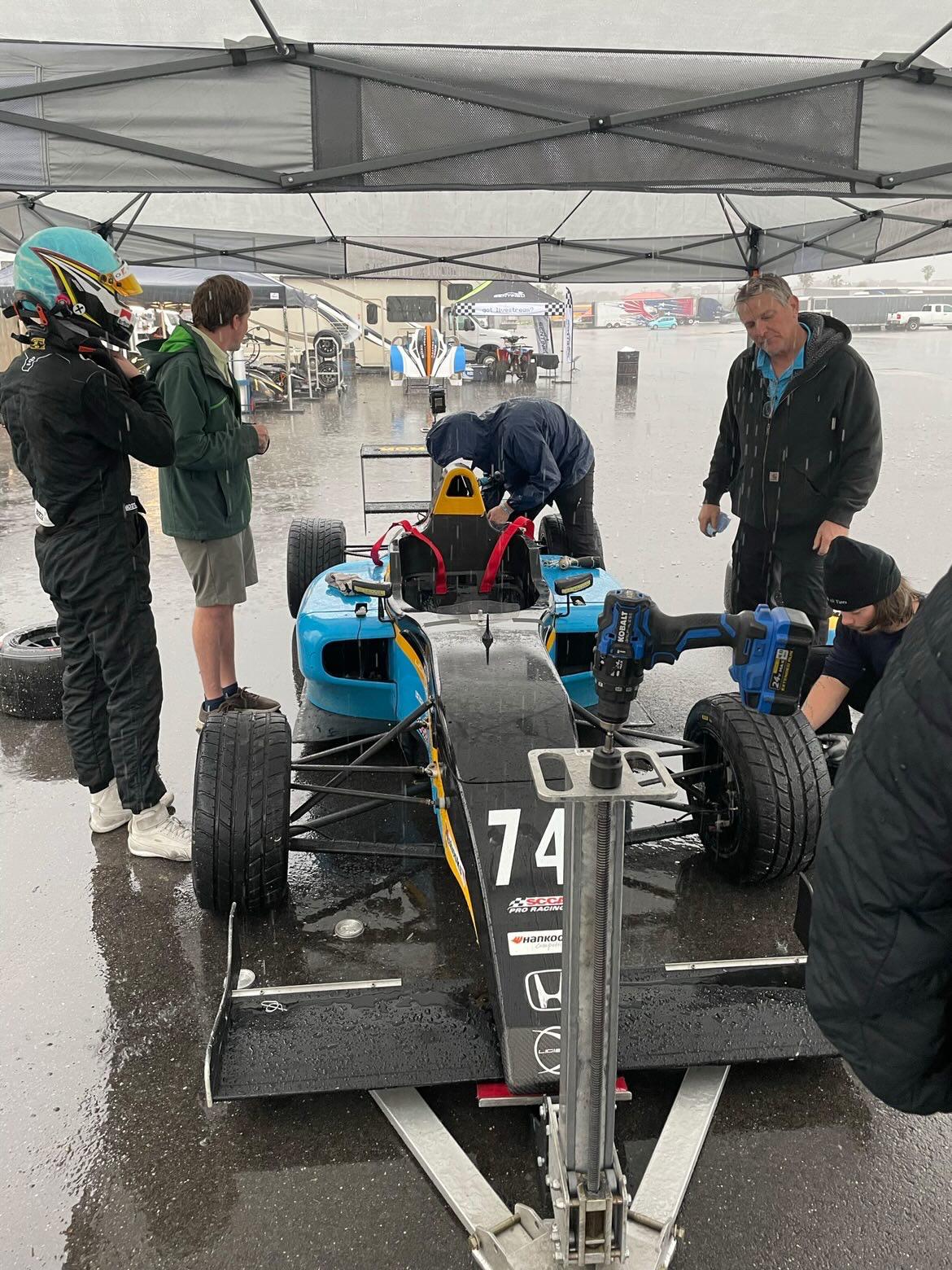 Garrett Dettman's car underneath a tent in the rain being serviced by mechanics