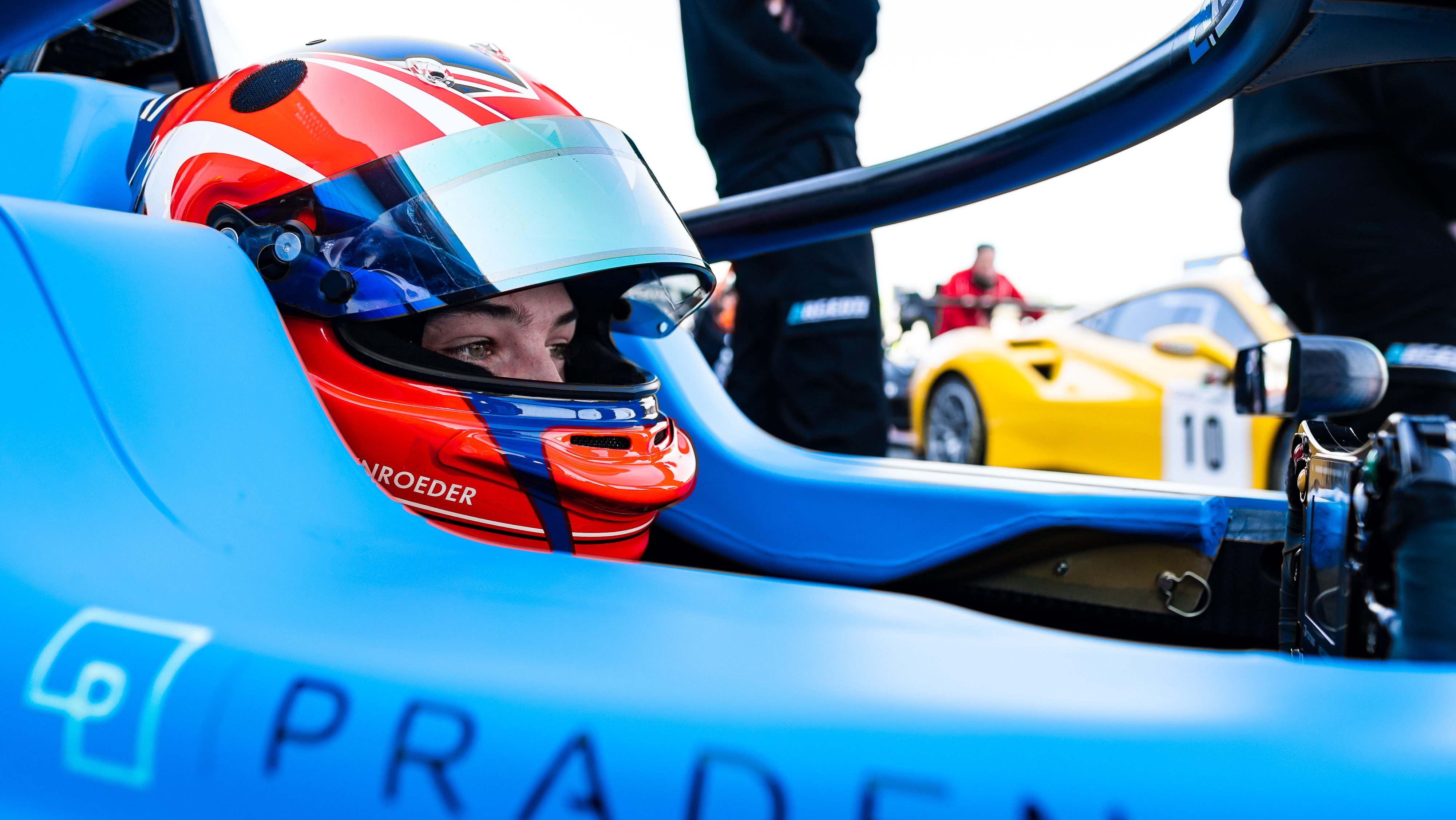 Driver in a red helmet sat in the cockpit of a blue race car