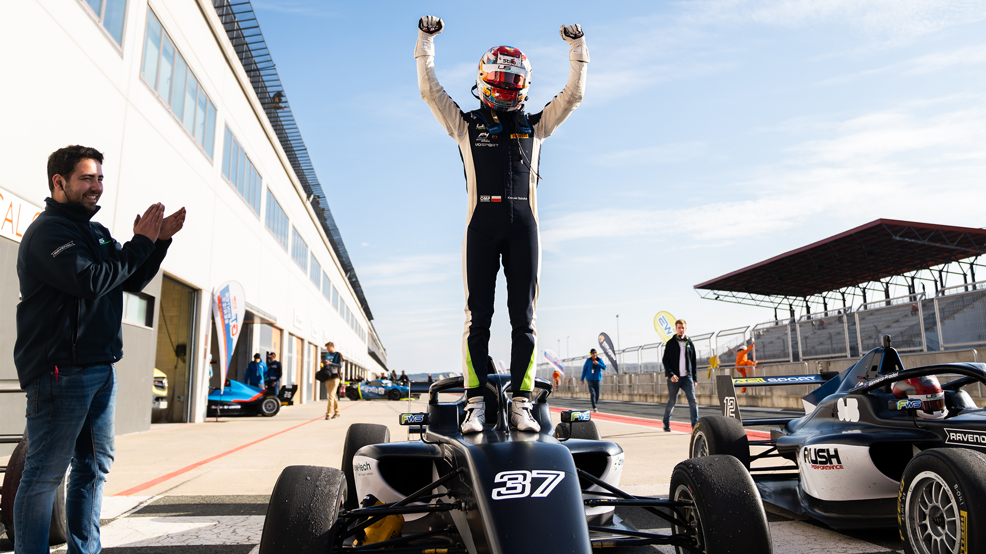 A driver stands on a black car with his fists raised