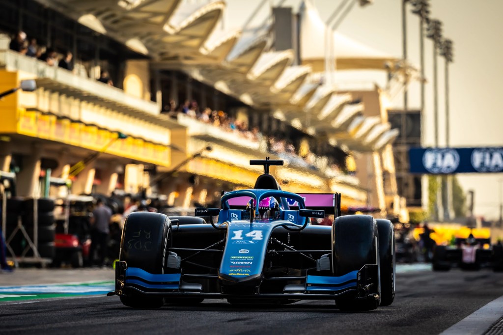 A blue and pink car on a yellow-hued, hazy pit lane, with a red car in the background