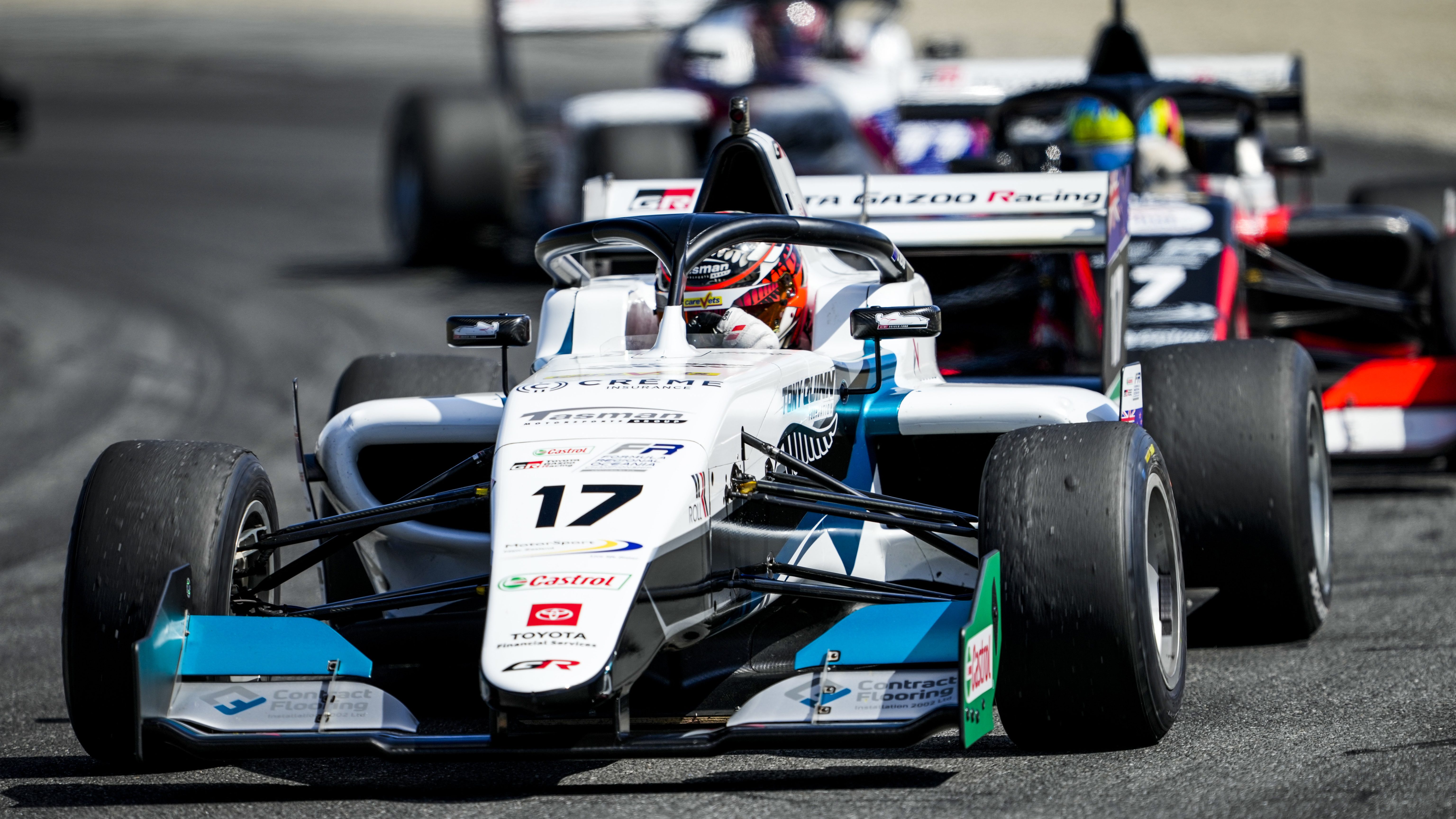 A white and blue FT-60 car preparing to turn right trailed by two other single-seaters