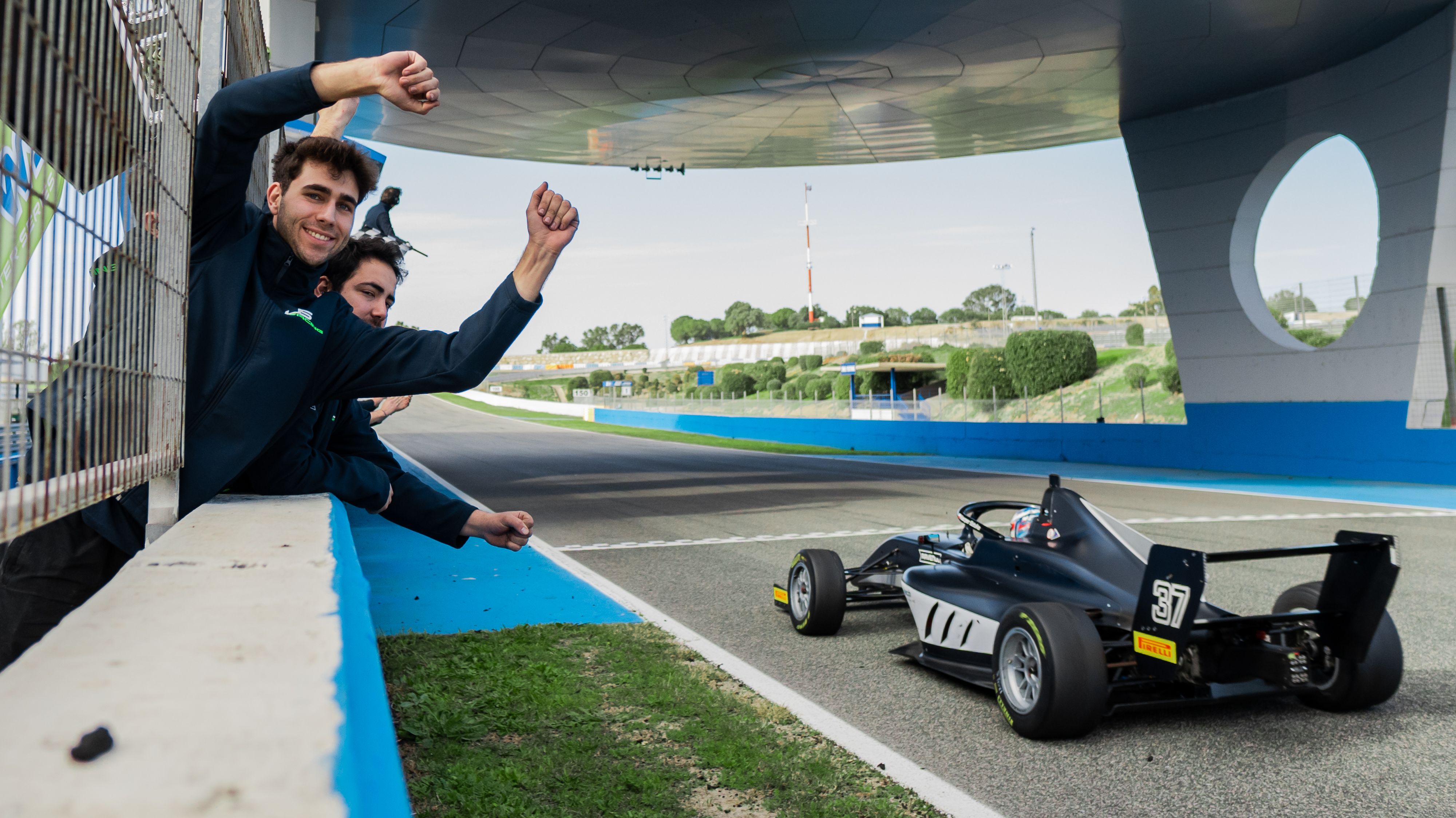 A black car crosses the line with mechanics, hands raised and facing the camera and the circuit, cheering the winning driver