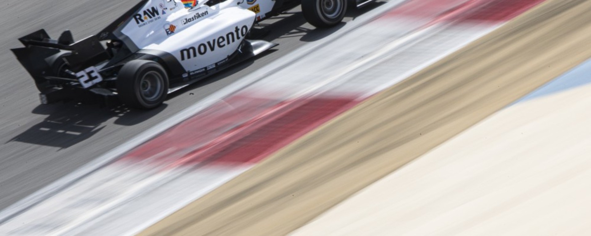 A white and black F3 car in the top-left corner of the image alongside a kerb, which blurs into the beige runoff to the bottom right