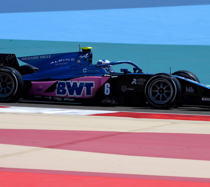 Blue, pink and black F2 car pointing to the right with blue runoff behind and red and beige runoff near to the camera