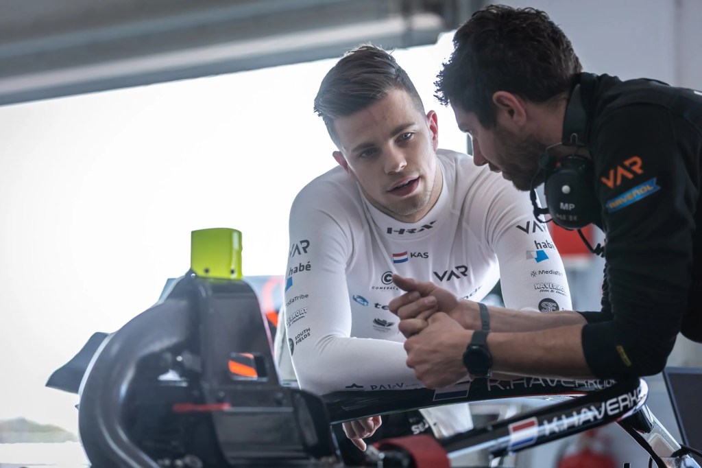 Kas Haverkort stands over the cockpit of his car talking to an engineer to his left