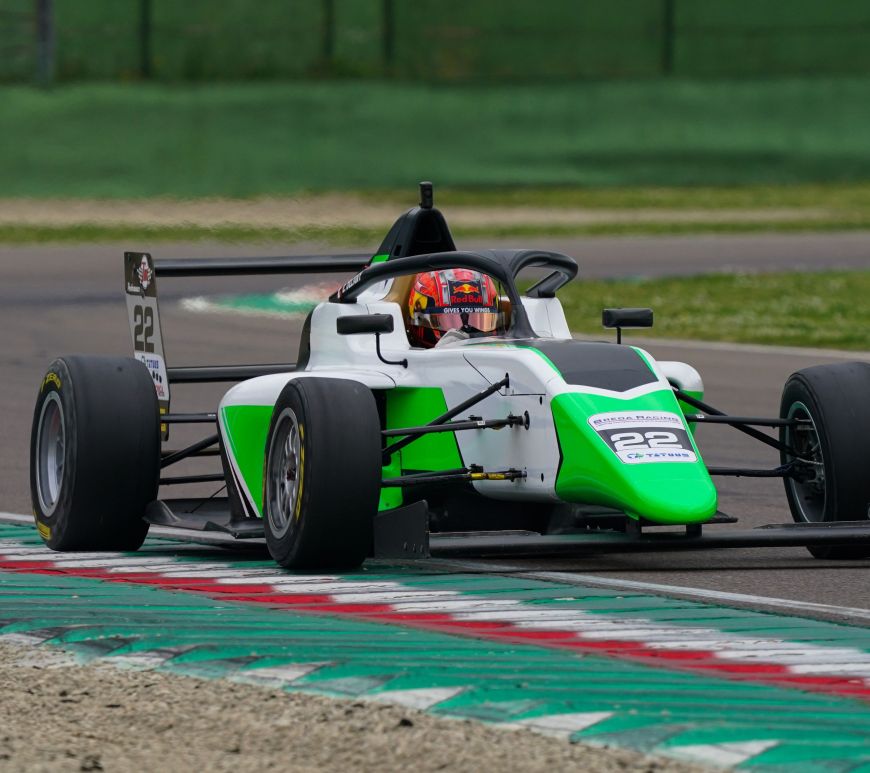 A green, white and black car with its right-side wheels against the rumble strips adorned with the Italian tricolore