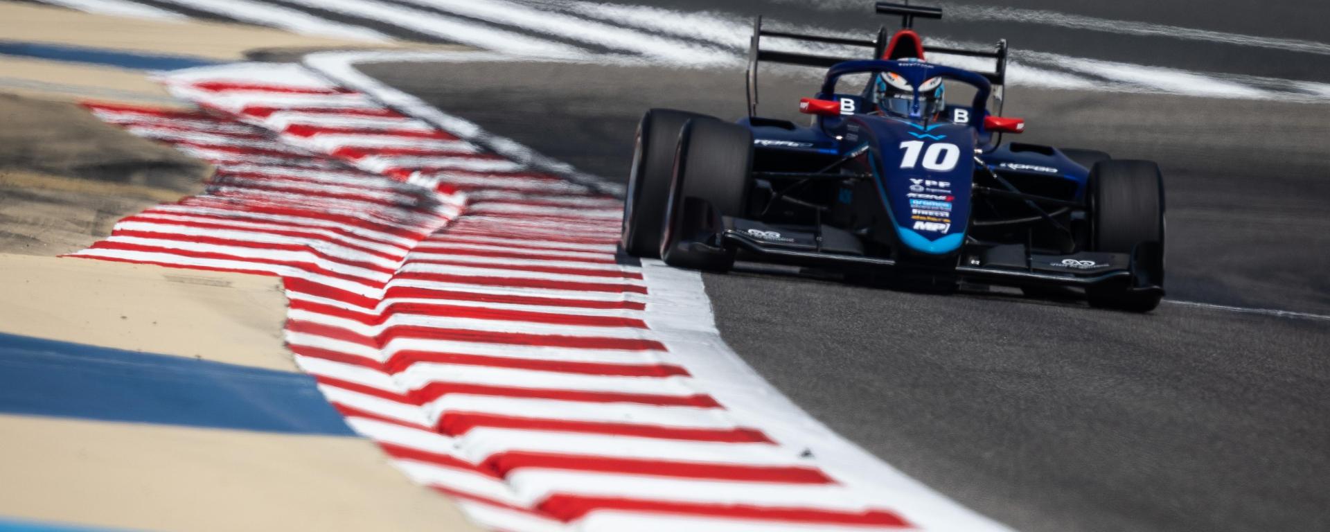 A blue F3 car facing the camera hugs the kerbs with the right-side tyres and DRS open