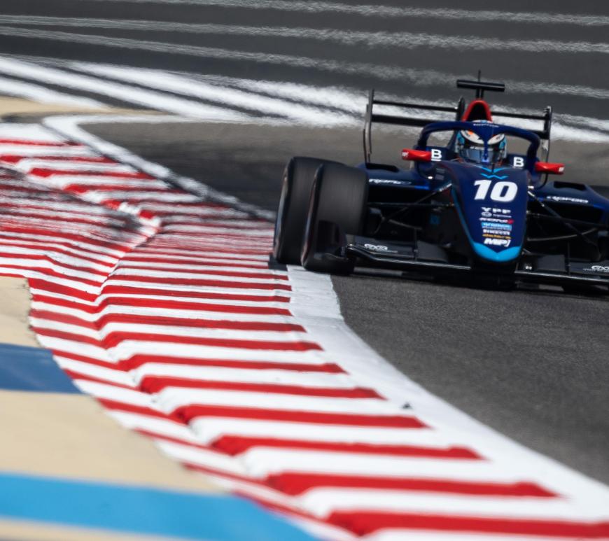 A blue F3 car facing the camera hugs the kerbs with the right-side tyres and DRS open