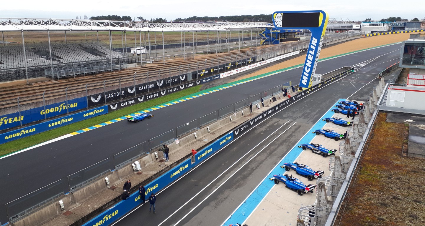 Overhead shot of the entrance to Turn 1 at the Bugatti Circuit, with cars in pit lane and one car on track