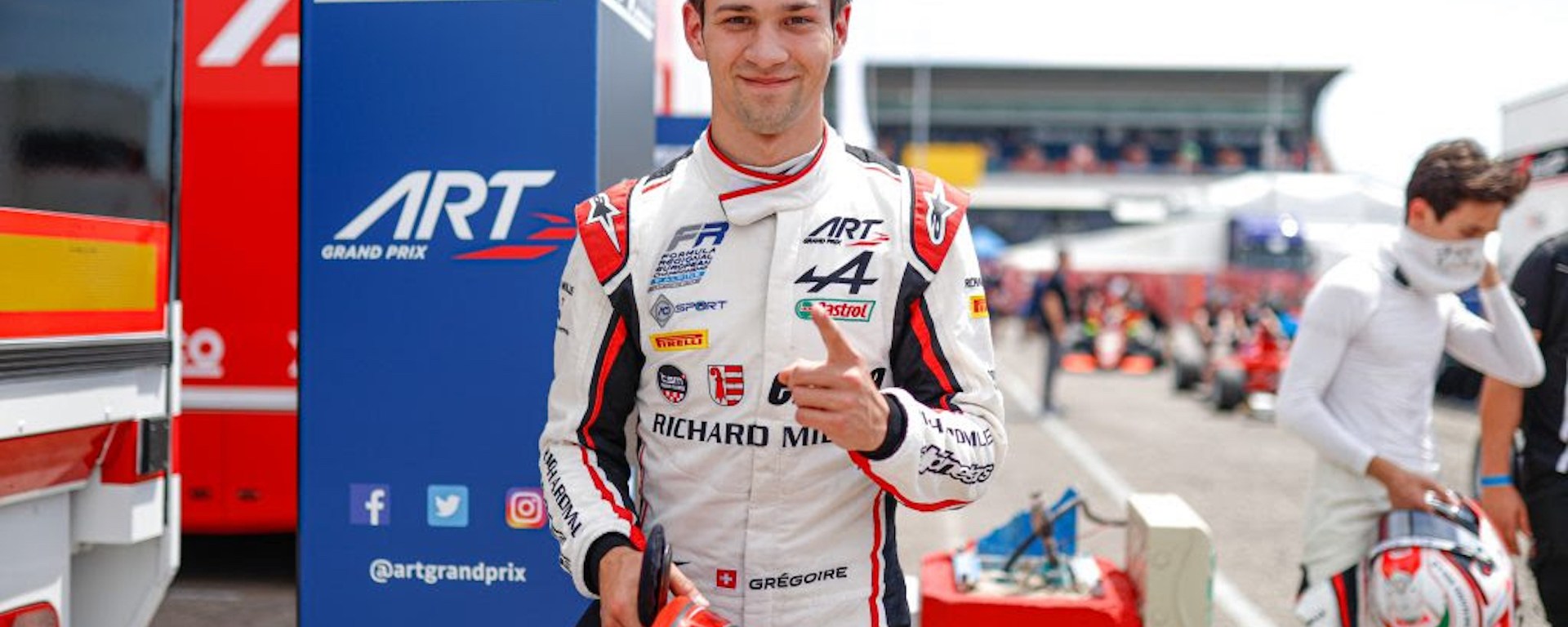 Grégoire Saucy points his left index finger while smiling at the camera and holding his helmet