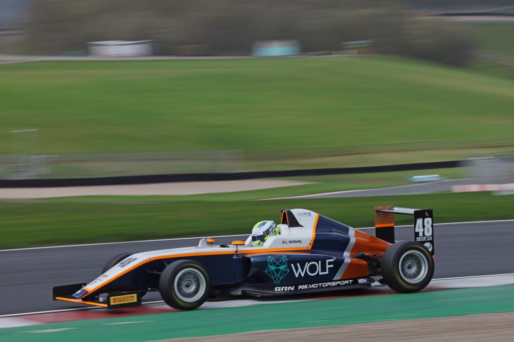 A blue, orange, and silver car on track photographed from the left