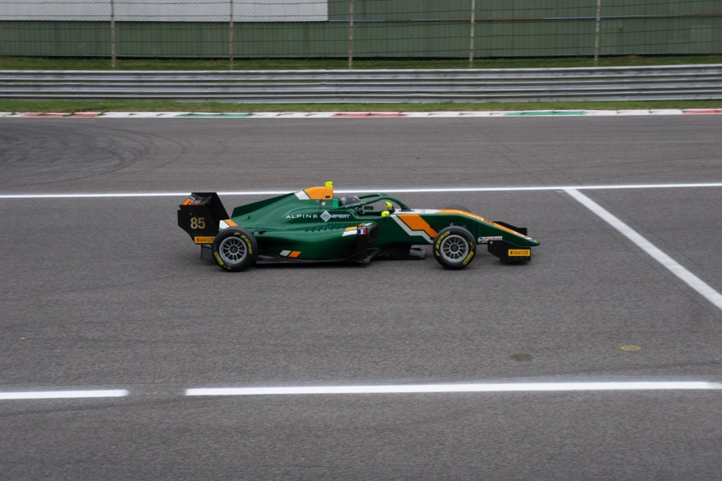 A green and orange car on track, shot from the right and facing to the right