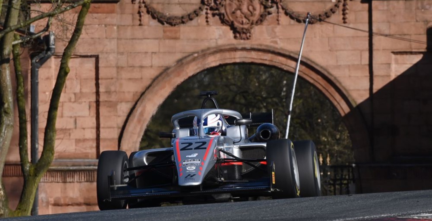 A silver car on a racetrack with an old bridge behind