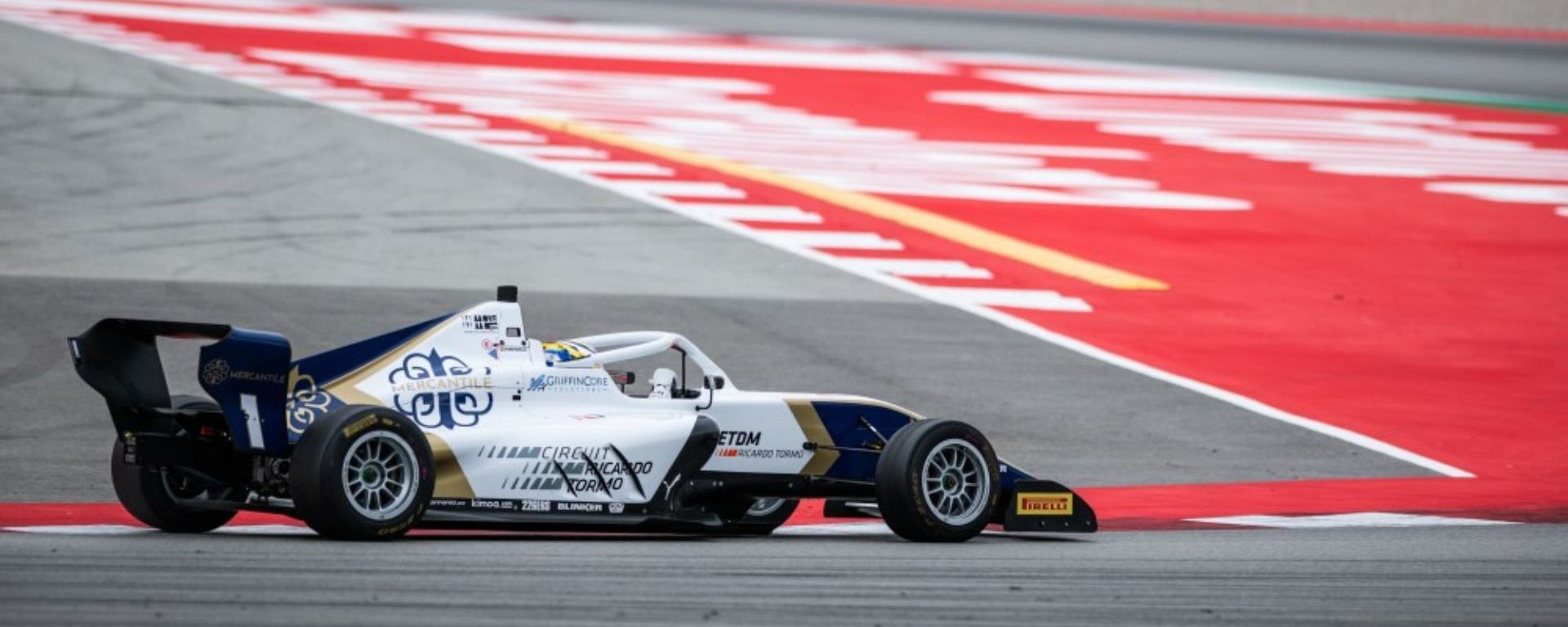 A white, gold and blue car turning left on the Circuit de Barcelona-Catalunya