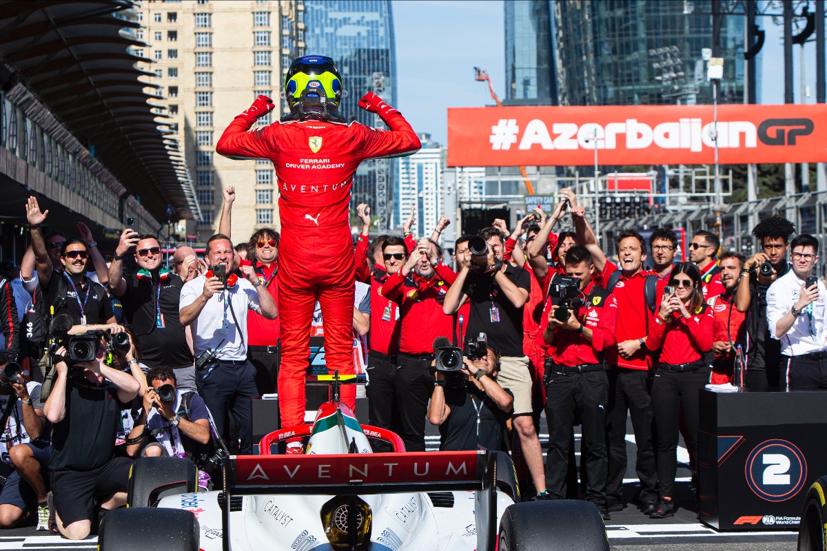 Ollie Bearman, photographed from the rear, standing on his car pumping his fists while the Prema team faces him celebrating
