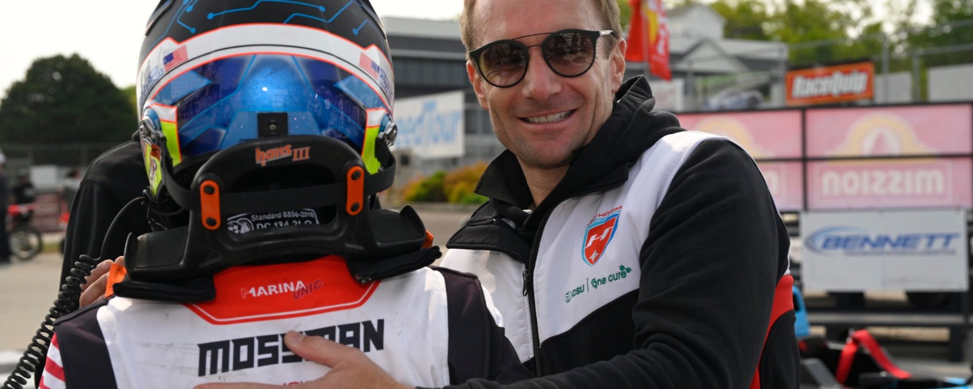 Jay Howard smiling at the camera while placing his hand on the back of Frankie Mossman, who is turned away from the camera