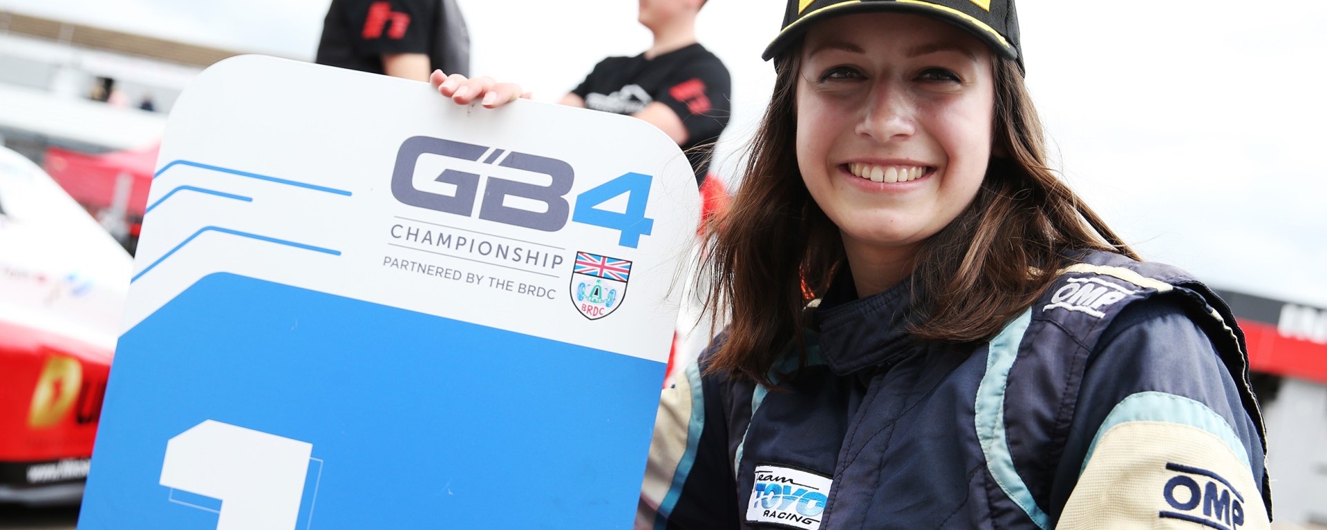 Megan Gilkes smiles while squatting beside a first-place board