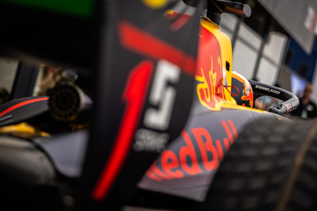 A navy blue and yellow racing car with the logo of a red bull lines up in the pit lane.