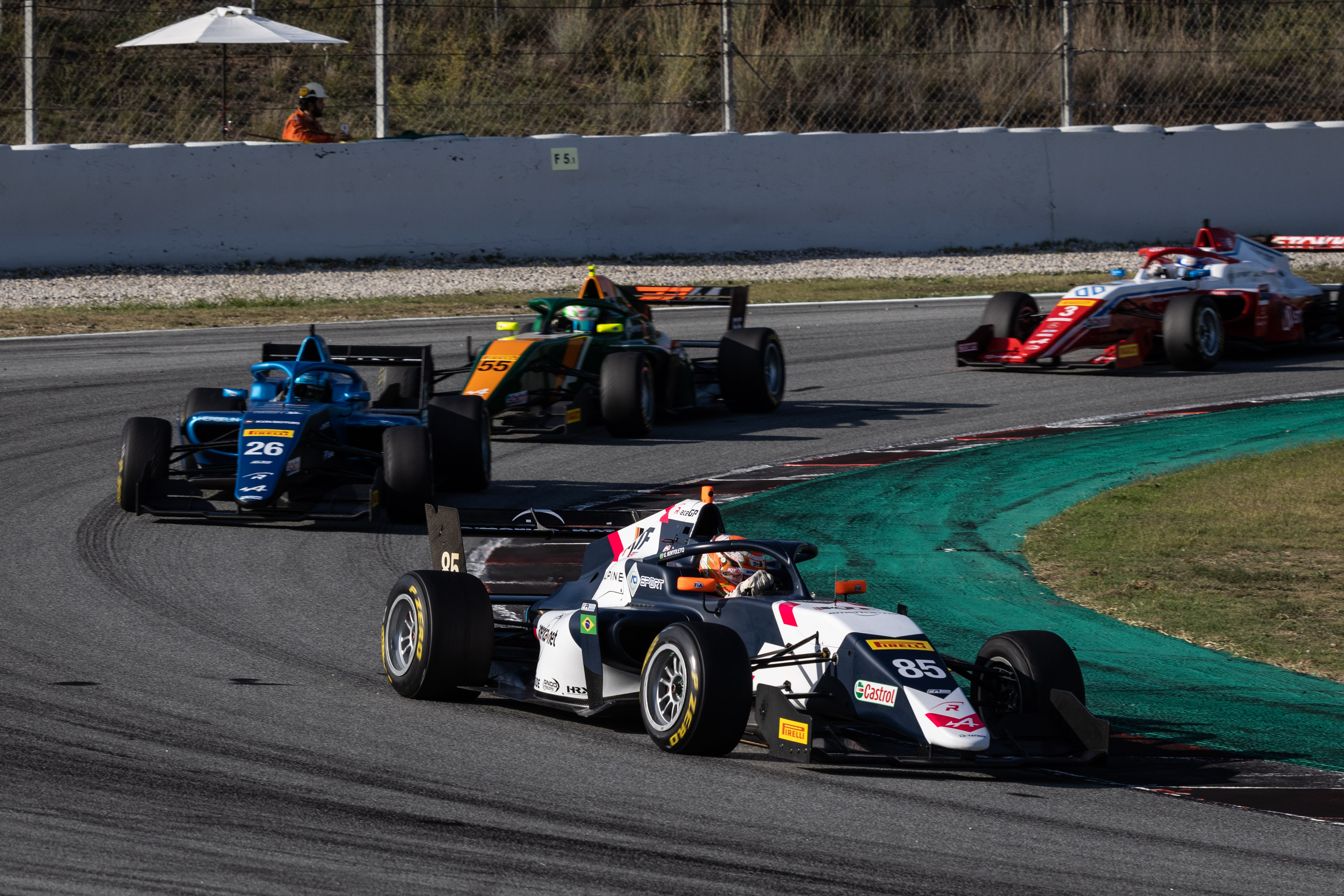 A white and black car turning left with a blue car, a green and orange car and a red car behind