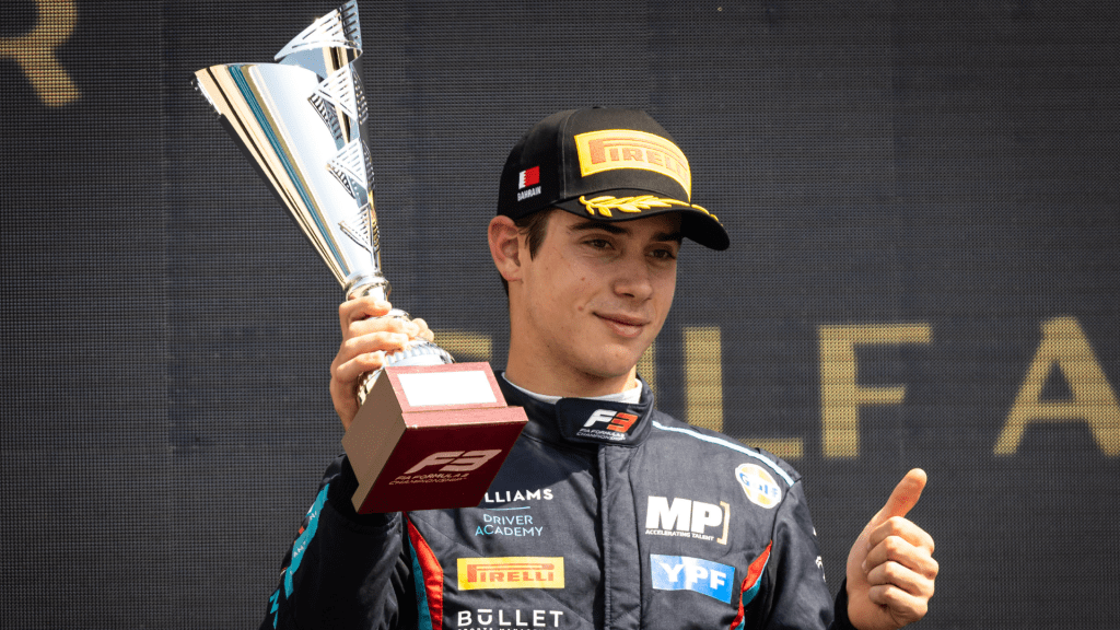 Franco Colapinto holding up a trophy in one hand and putting his other hand's thumb up