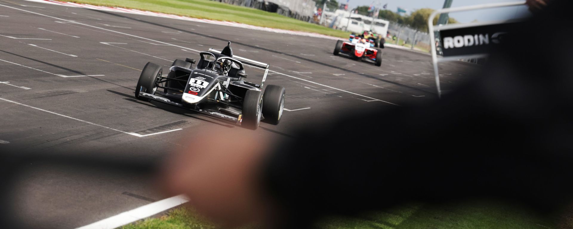 A black and white car driving towards pit boards to take the chequered flag