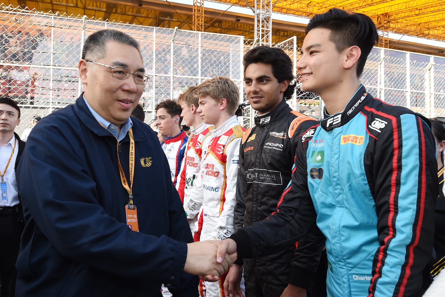 A man in a blue jacket shakes hands with a racing driver in a blue suit